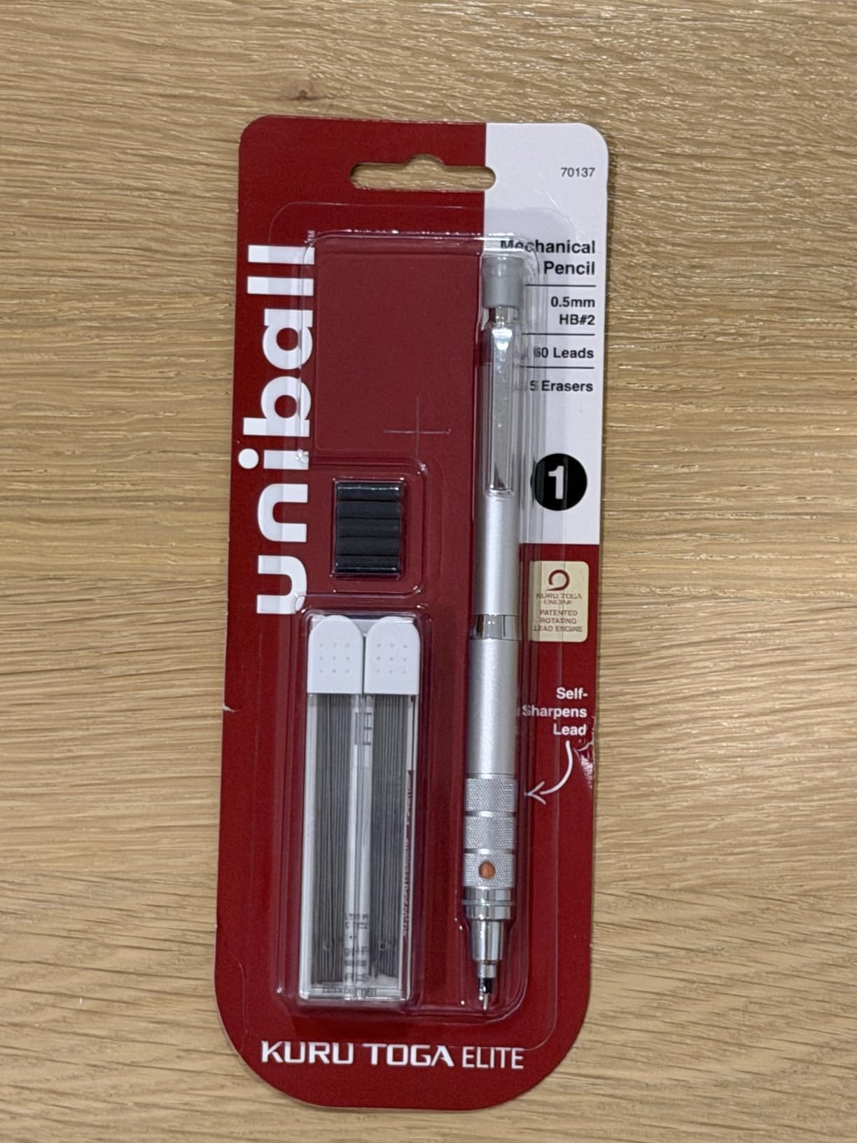 Sealed uniball Kuru Toga Elite blister pack, item 70137, on a light wood table with 60 leads and 5 erasers beside the silver pencil