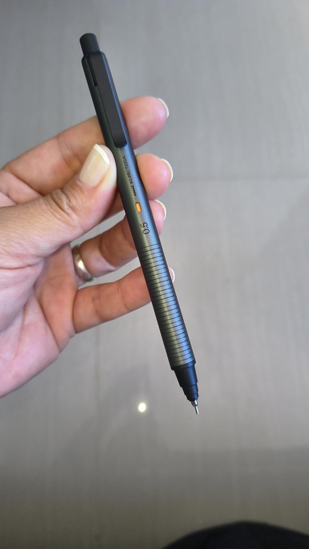 Kuru Toga Metal in Phantom Gray held between two fingers, the orange engine window and the 0.5 marking sitting above the ribbed grip